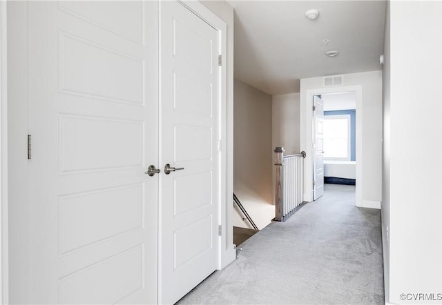 hallway featuring light colored carpet, visible vents, and baseboards