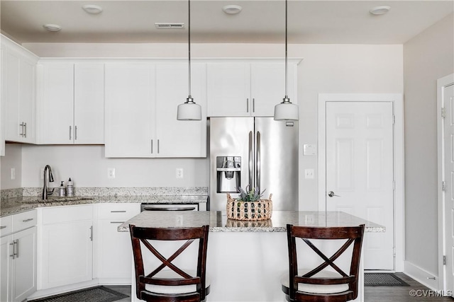 kitchen featuring visible vents, stainless steel fridge with ice dispenser, a kitchen bar, white cabinets, and a sink