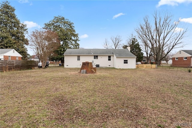 rear view of house with a yard, a chimney, and fence