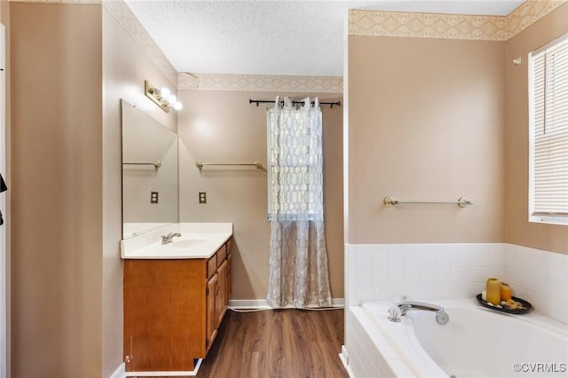 full bath featuring a textured ceiling, vanity, a garden tub, and wood finished floors