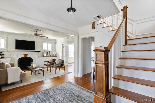 living area with visible vents, stairs, a fireplace, ceiling fan, and dark wood-style flooring