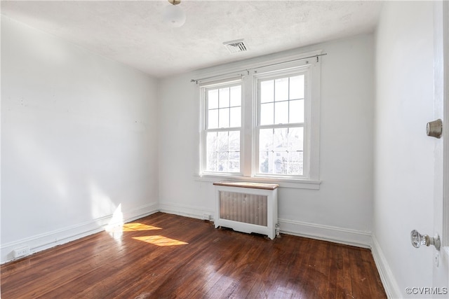 spare room featuring visible vents, radiator, baseboards, hardwood / wood-style floors, and a textured ceiling