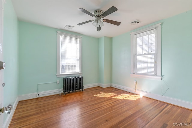 empty room featuring visible vents, radiator, baseboards, and wood finished floors