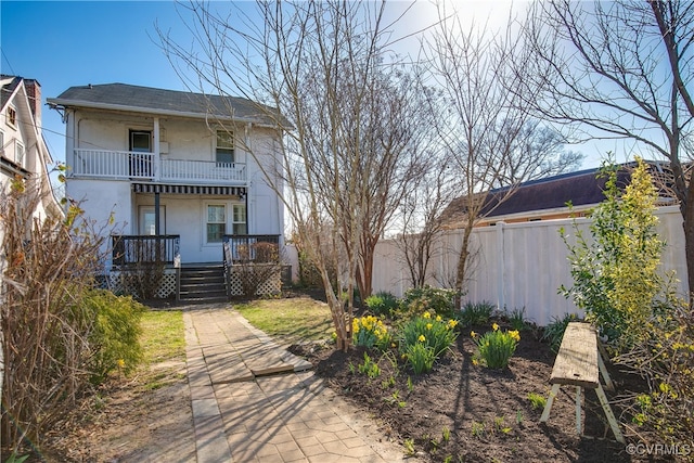 exterior space featuring stucco siding, a balcony, covered porch, and fence