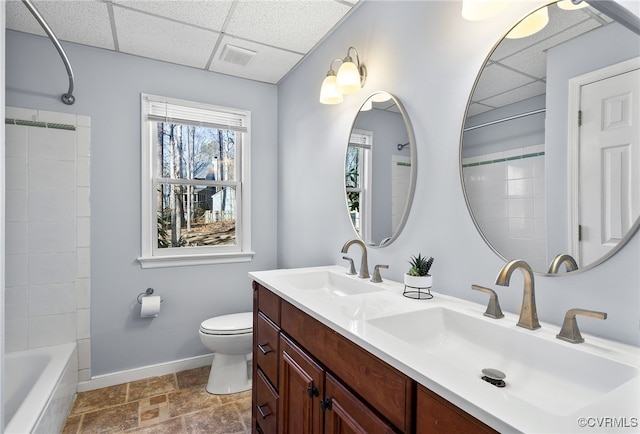 full bath with toilet, a paneled ceiling, baseboards, and a sink