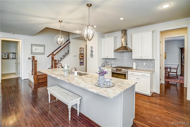 kitchen with wall chimney range hood, a sink, a kitchen breakfast bar, stainless steel gas stove, and backsplash