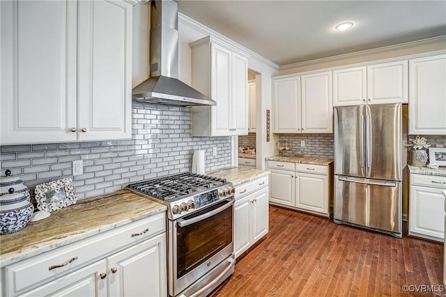 kitchen with wall chimney range hood, decorative backsplash, appliances with stainless steel finishes, wood finished floors, and white cabinetry