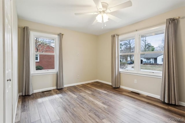 empty room featuring a ceiling fan, light wood-style floors, visible vents, and baseboards