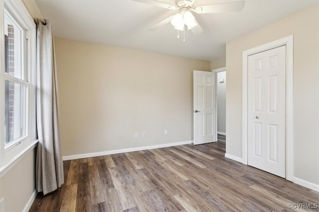 unfurnished bedroom featuring wood finished floors, baseboards, a closet, and ceiling fan