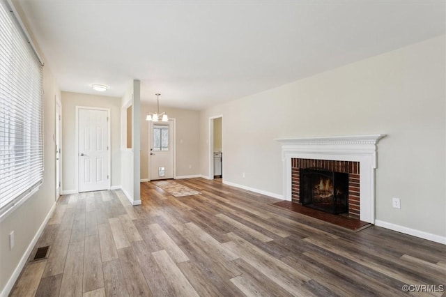 unfurnished living room featuring visible vents, a notable chandelier, wood finished floors, a fireplace, and baseboards