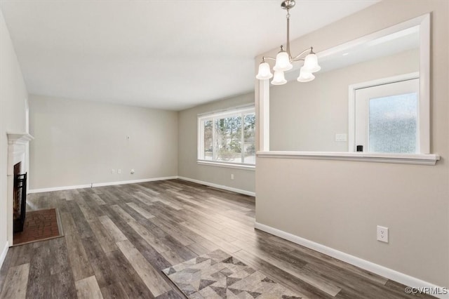 unfurnished living room featuring a notable chandelier, a fireplace with raised hearth, baseboards, and wood finished floors