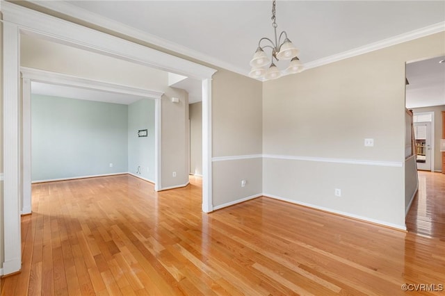 empty room with a notable chandelier, baseboards, light wood finished floors, and ornamental molding