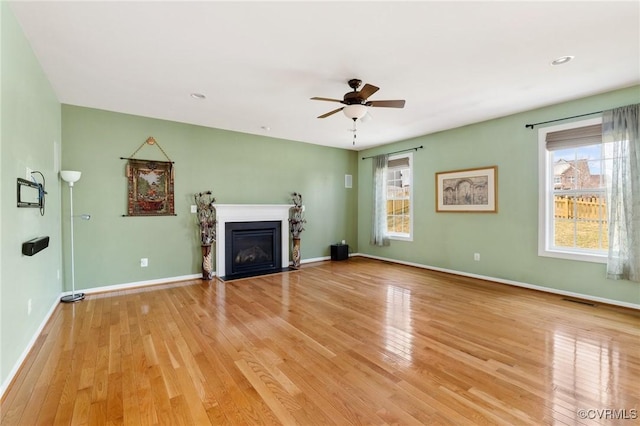 unfurnished living room featuring a wealth of natural light, baseboards, a fireplace with flush hearth, and light wood-style flooring