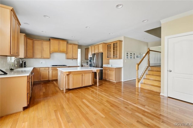 kitchen featuring light wood-type flooring, a kitchen island, gas stovetop, stainless steel fridge, and light countertops