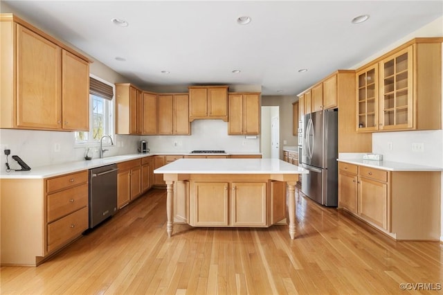 kitchen with light wood finished floors, a sink, a kitchen island, appliances with stainless steel finishes, and light countertops