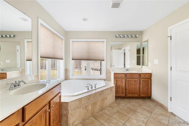 bathroom with visible vents, two vanities, a sink, a garden tub, and tile patterned floors