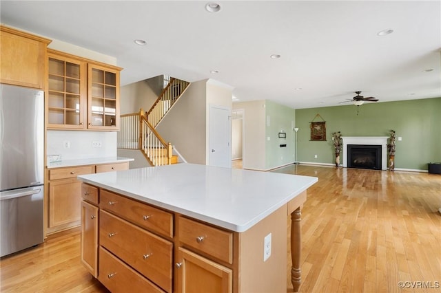 kitchen with light wood finished floors, a kitchen island, light countertops, a fireplace, and freestanding refrigerator