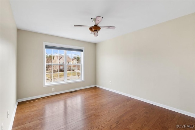 empty room with ceiling fan, visible vents, baseboards, and wood finished floors