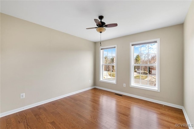 empty room with a ceiling fan, wood finished floors, visible vents, and baseboards