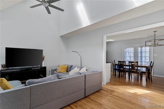 living area with ceiling fan with notable chandelier, light wood-type flooring, and baseboards