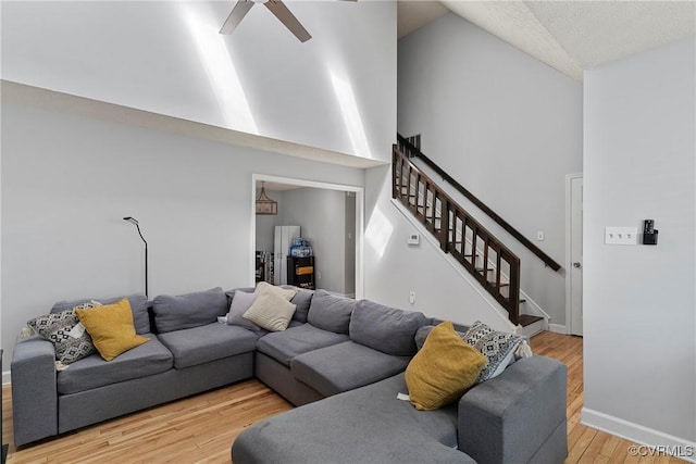 living area featuring a ceiling fan, baseboards, light wood finished floors, high vaulted ceiling, and stairs