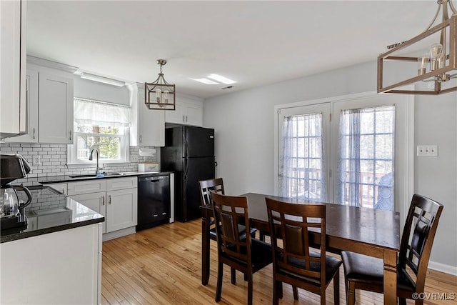 kitchen featuring black appliances, a sink, tasteful backsplash, dark countertops, and light wood-style floors