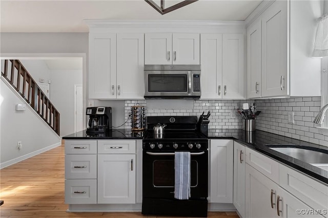 kitchen featuring dark countertops, stainless steel microwave, black electric range, white cabinetry, and a sink