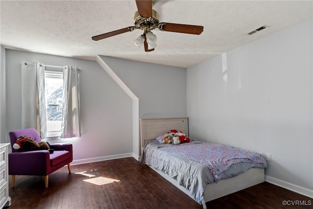 bedroom featuring a ceiling fan, wood finished floors, visible vents, baseboards, and a textured ceiling