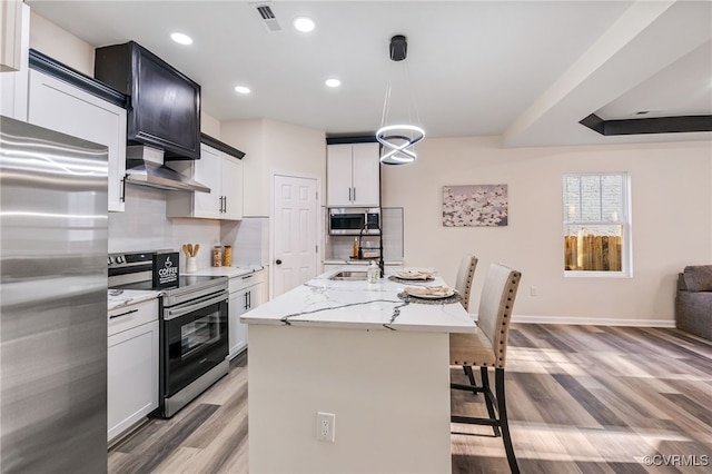 kitchen featuring visible vents, appliances with stainless steel finishes, a kitchen breakfast bar, wall chimney exhaust hood, and a sink