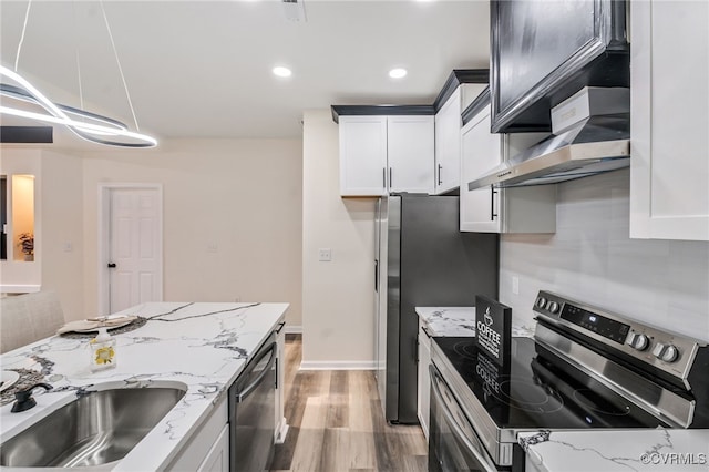 kitchen with light stone countertops, a sink, white cabinets, under cabinet range hood, and appliances with stainless steel finishes