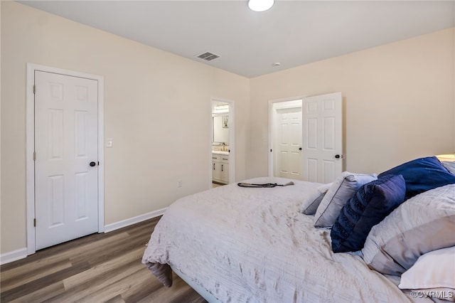 bedroom featuring visible vents, a sink, ensuite bath, wood finished floors, and baseboards