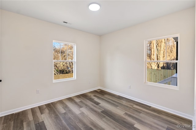 spare room with dark wood-style floors, visible vents, and baseboards