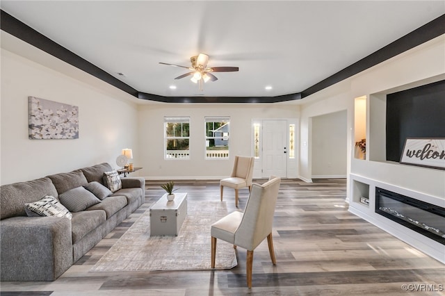 living area with a glass covered fireplace, baseboards, wood finished floors, and ceiling fan