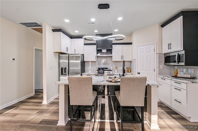 kitchen featuring pendant lighting, decorative backsplash, wood finished floors, stainless steel appliances, and a kitchen island with sink