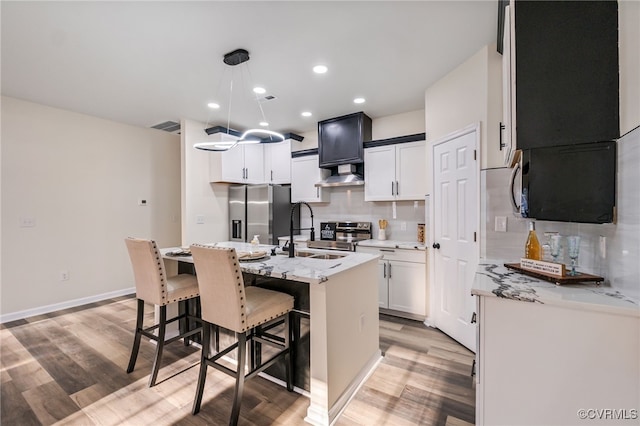 kitchen featuring ventilation hood, visible vents, a sink, decorative backsplash, and appliances with stainless steel finishes