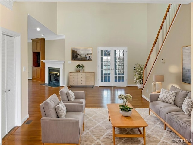 living room featuring a fireplace with flush hearth, light wood-style flooring, french doors, and a towering ceiling