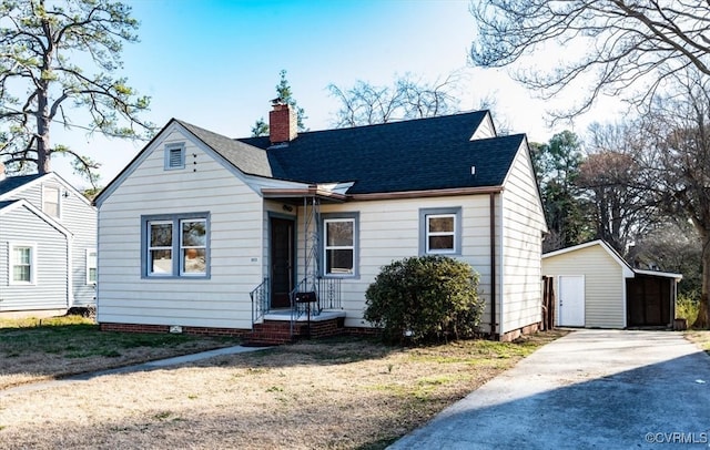 bungalow-style house with a chimney, an outdoor structure, and a shingled roof