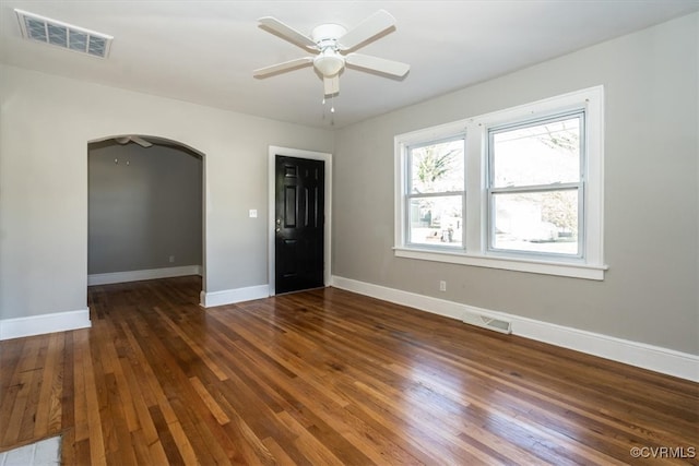 unfurnished room featuring visible vents, arched walkways, baseboards, and wood-type flooring