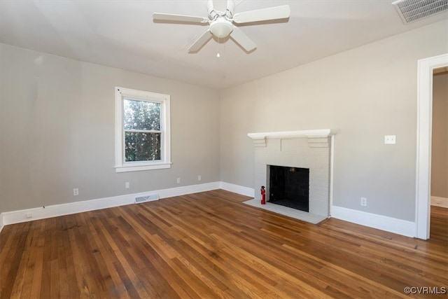 unfurnished living room with a brick fireplace, wood finished floors, visible vents, and baseboards