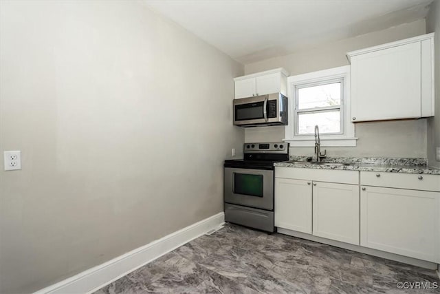 kitchen featuring light stone counters, baseboards, a sink, appliances with stainless steel finishes, and white cabinetry