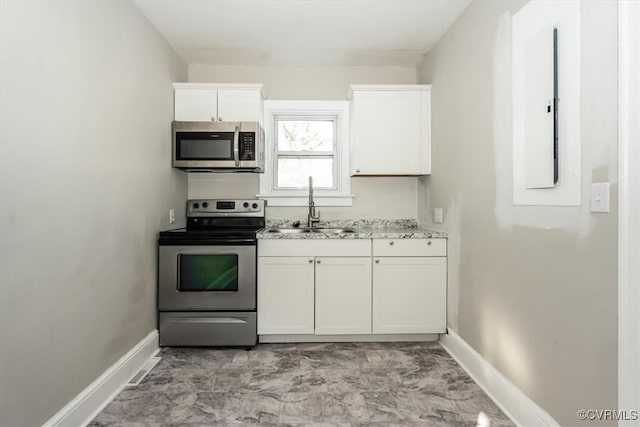 kitchen featuring light stone countertops, baseboards, a sink, appliances with stainless steel finishes, and white cabinetry