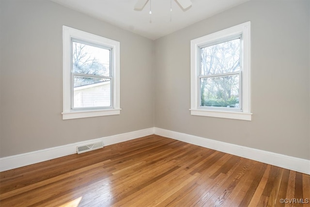 spare room featuring visible vents, a healthy amount of sunlight, baseboards, and wood-type flooring