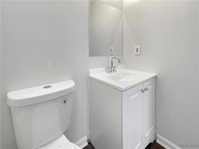 half bathroom with vanity, toilet, and baseboards