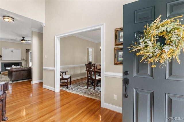 foyer with crown molding, baseboards, a fireplace, light wood-style floors, and a ceiling fan