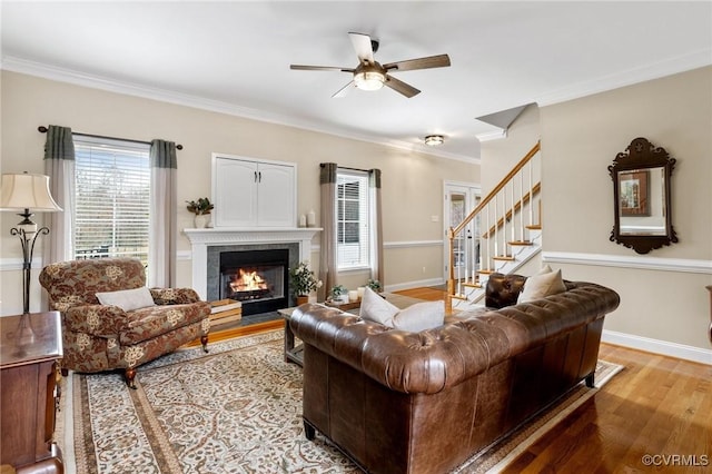 living room featuring crown molding, baseboards, stairway, a fireplace with flush hearth, and light wood-style flooring