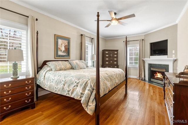 bedroom featuring a fireplace with flush hearth, wood finished floors, a ceiling fan, and ornamental molding