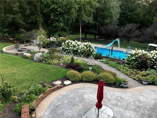 view of swimming pool with a fire pit, a water slide, fence, a lawn, and a patio