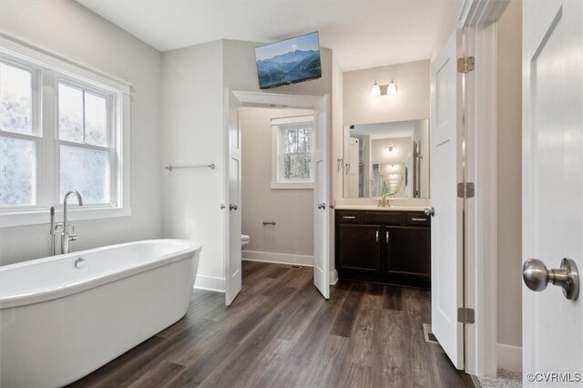 full bath with a freestanding tub, toilet, wood finished floors, and vanity