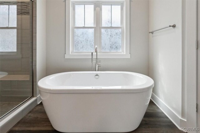 bathroom featuring a shower stall, wood finished floors, baseboards, and a freestanding bath