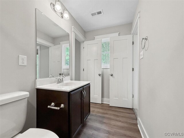 half bathroom with vanity, wood finished floors, visible vents, baseboards, and toilet